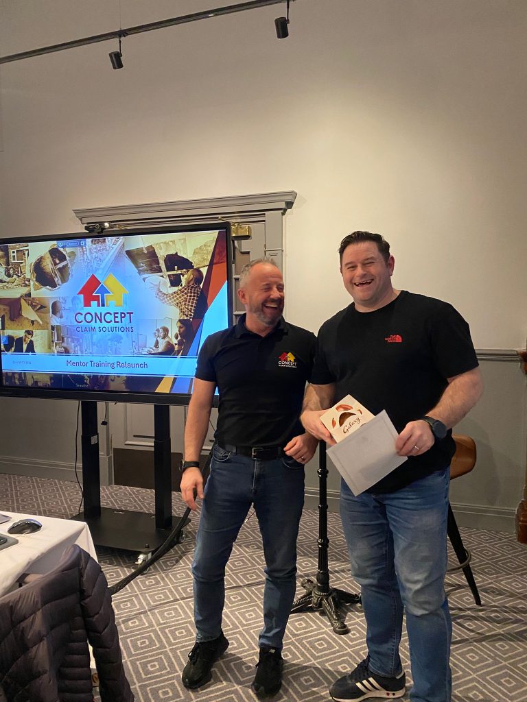 Two men laughing beside a Concept Claim Solutions mentor training screen